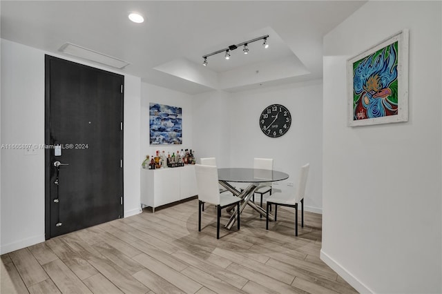 dining room with light hardwood / wood-style flooring, track lighting, and a tray ceiling