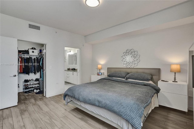 bedroom with a spacious closet, ensuite bath, a closet, and hardwood / wood-style flooring