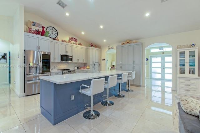 kitchen featuring lofted ceiling, appliances with stainless steel finishes, a breakfast bar, a spacious island, and light stone countertops