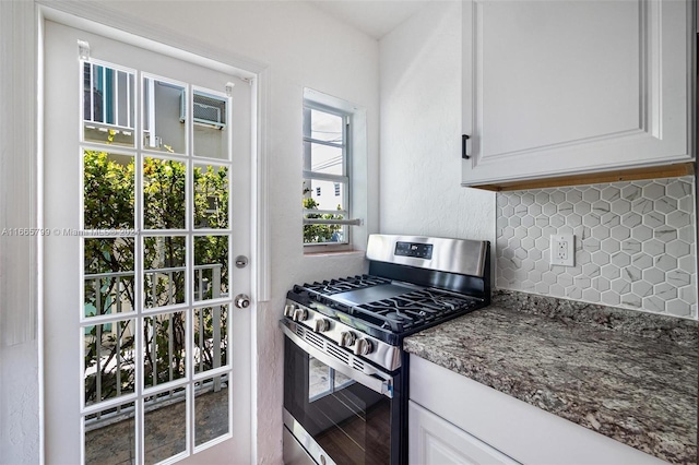 kitchen with tasteful backsplash, stainless steel gas range, white cabinetry, dark stone countertops, and hardwood / wood-style floors