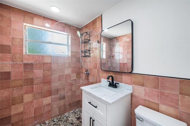 bathroom featuring tile walls, tiled shower, vanity, and toilet