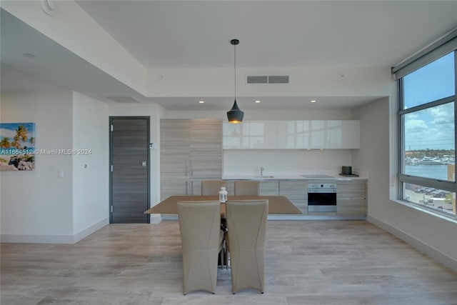 kitchen featuring pendant lighting, oven, white cabinetry, light hardwood / wood-style floors, and a water view