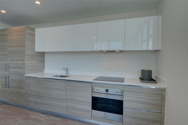 kitchen featuring black electric cooktop, white cabinetry, stainless steel oven, light hardwood / wood-style flooring, and sink