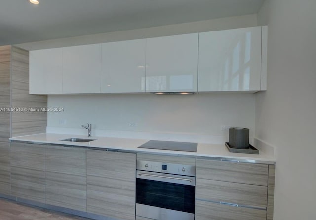 kitchen featuring white cabinetry, stainless steel oven, light wood-type flooring, black electric stovetop, and sink