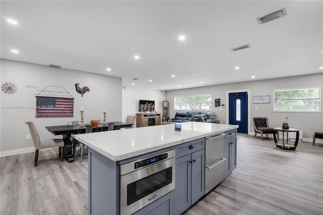 kitchen with stainless steel microwave, light stone counters, gray cabinetry, and a kitchen island