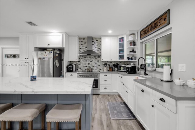 kitchen with wall chimney range hood, white cabinetry, and appliances with stainless steel finishes