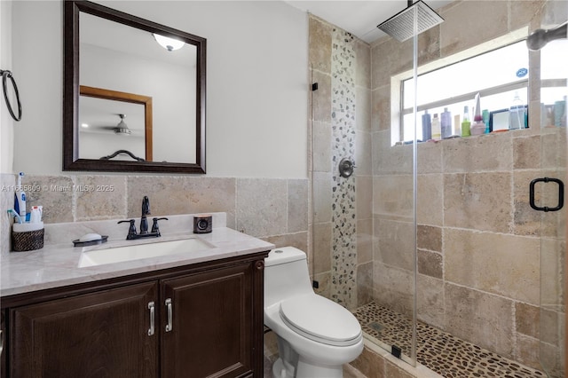 bathroom with tile walls, vanity, a shower with door, and toilet