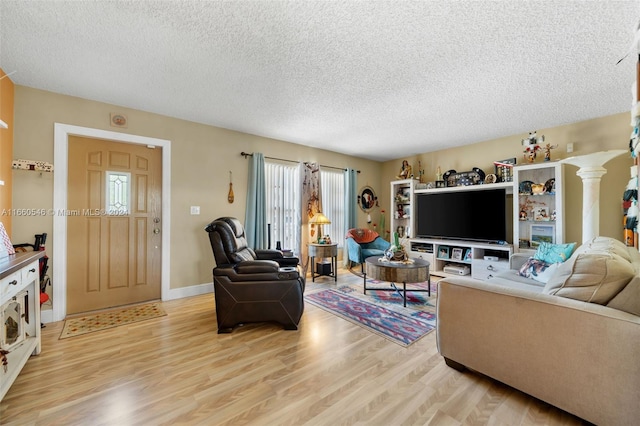 living room featuring light hardwood / wood-style flooring, decorative columns, and a textured ceiling