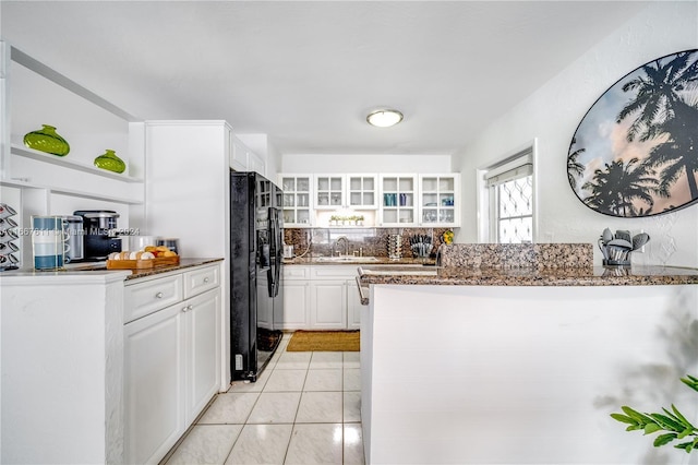 kitchen featuring backsplash, black fridge, sink, light tile patterned floors, and white cabinetry