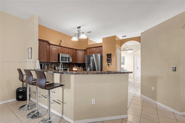 kitchen with decorative backsplash, light tile patterned flooring, kitchen peninsula, stainless steel appliances, and a chandelier