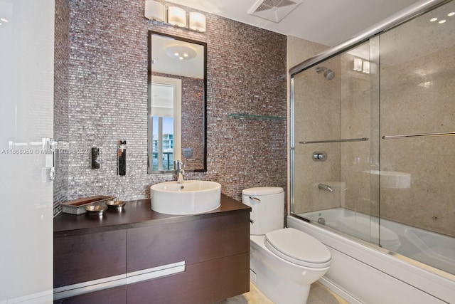 full bathroom with tile walls, vanity, toilet, and bath / shower combo with glass door