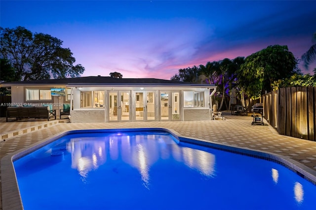 pool at dusk with french doors and a patio