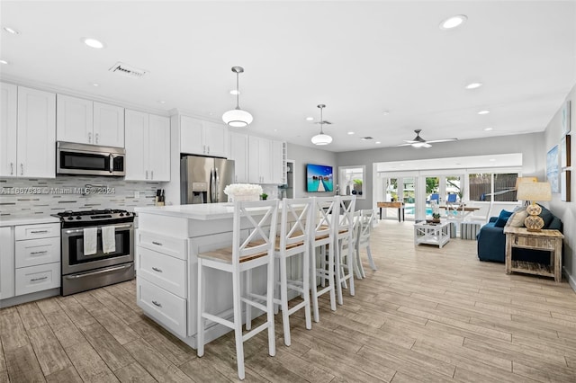 kitchen featuring appliances with stainless steel finishes, white cabinetry, a kitchen island, light wood-type flooring, and french doors