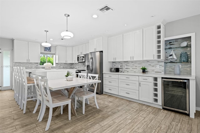 kitchen with pendant lighting, stainless steel appliances, white cabinetry, and beverage cooler