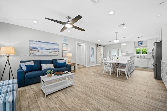 living room featuring a barn door, sink, ceiling fan, and light hardwood / wood-style flooring