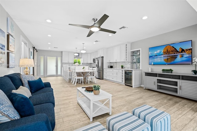 living room with ceiling fan, wine cooler, and light wood-type flooring