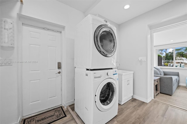 clothes washing area with cabinets, light hardwood / wood-style floors, and stacked washer / drying machine