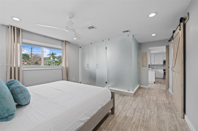 bedroom featuring a barn door, ceiling fan, and light hardwood / wood-style flooring