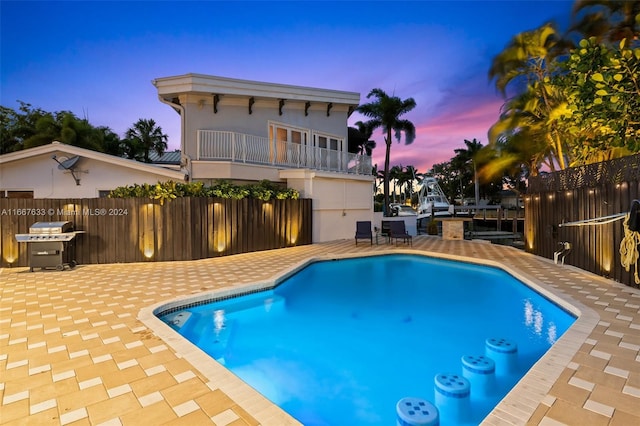 pool at dusk featuring area for grilling and a patio area