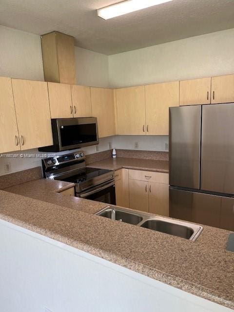 kitchen featuring light brown cabinetry, stone counters, stainless steel appliances, and a sink