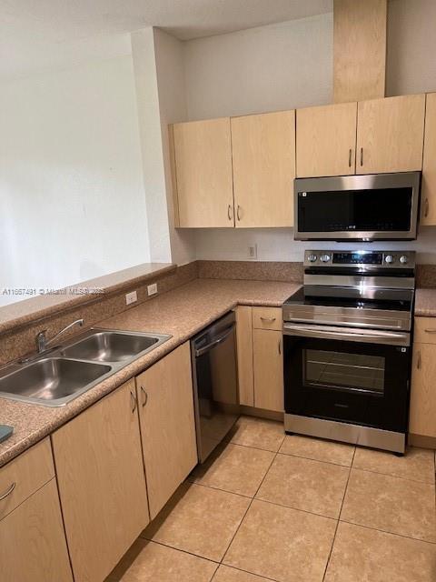 kitchen with a sink, appliances with stainless steel finishes, light brown cabinets, and light tile patterned floors