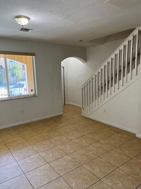 empty room with stairway, light tile patterned floors, baseboards, arched walkways, and a textured ceiling