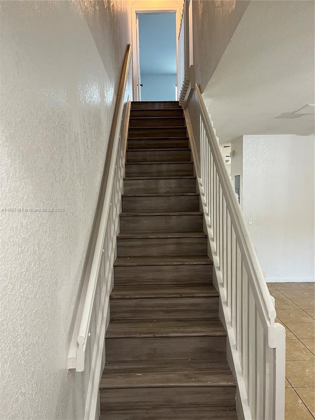 stairway featuring tile patterned flooring and a textured wall