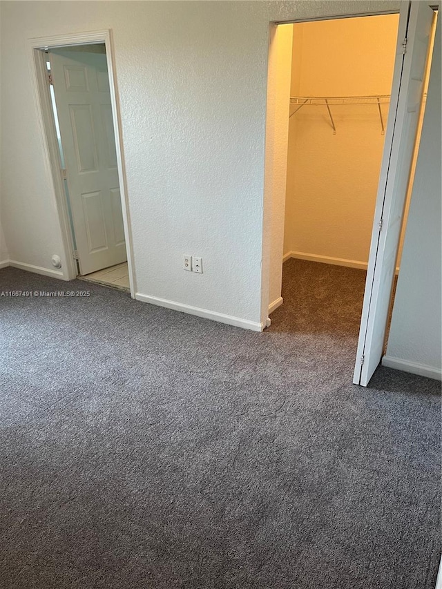 unfurnished bedroom featuring a spacious closet, baseboards, a closet, and carpet floors