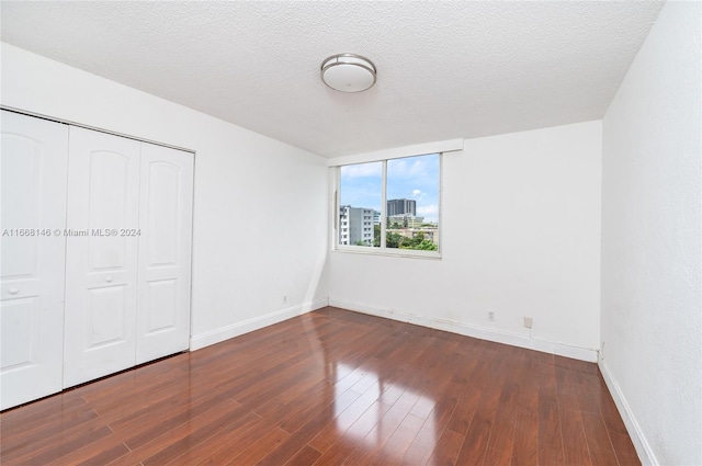 unfurnished bedroom featuring a textured ceiling, a closet, and dark hardwood / wood-style flooring