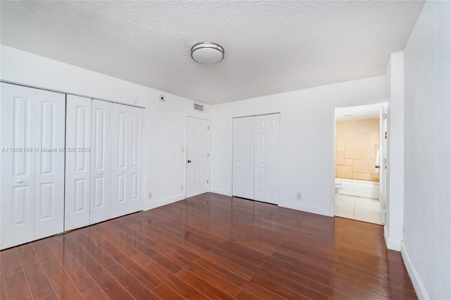 unfurnished bedroom with ensuite bathroom, multiple closets, a textured ceiling, and dark hardwood / wood-style floors