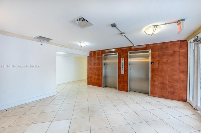 spare room with tile walls, elevator, and light tile patterned floors