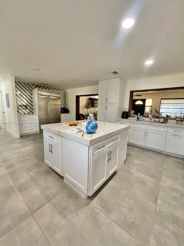 kitchen with a kitchen island, white cabinetry, stainless steel built in refrigerator, sink, and light stone countertops