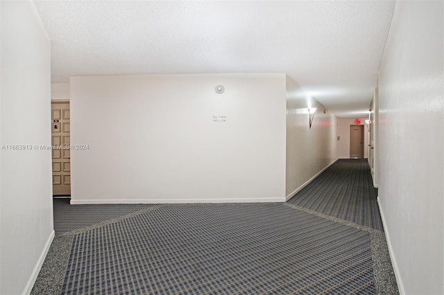 hall with a textured ceiling and dark colored carpet