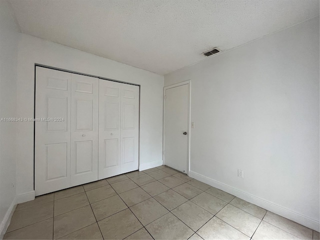 unfurnished bedroom featuring a textured ceiling, a closet, and light tile patterned floors