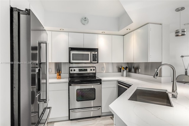 kitchen with pendant lighting, sink, white cabinets, appliances with stainless steel finishes, and light stone countertops