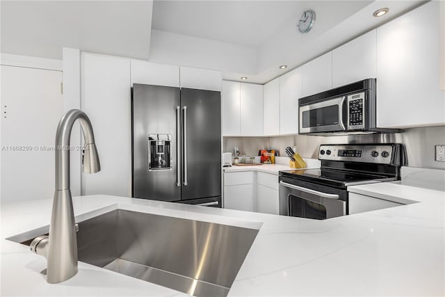 kitchen with light stone counters, white cabinets, stainless steel appliances, and sink