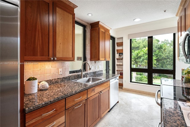 kitchen with a textured ceiling, tasteful backsplash, sink, stainless steel appliances, and dark stone countertops