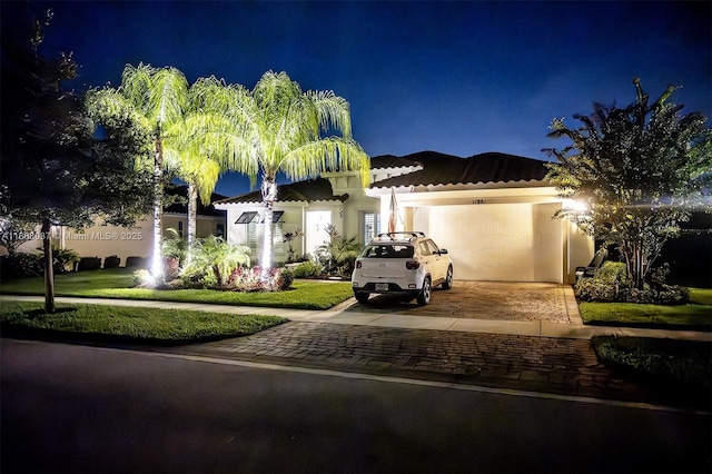 mediterranean / spanish-style home featuring an attached garage, decorative driveway, a tile roof, and stucco siding