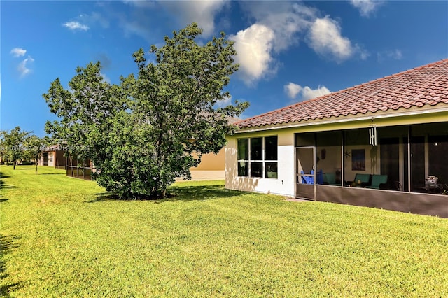 back of property featuring stucco siding, a sunroom, a tiled roof, and a lawn