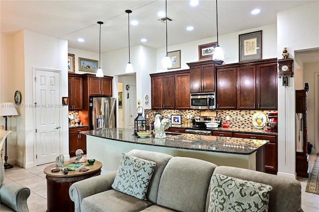 kitchen featuring a kitchen island with sink, light tile patterned flooring, appliances with stainless steel finishes, and decorative light fixtures