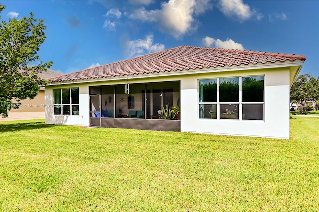 rear view of property featuring a yard, a sunroom, stucco siding, and a tile roof