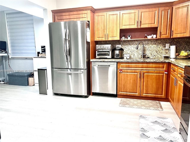 kitchen featuring sink, light stone counters, tasteful backsplash, light wood-type flooring, and stainless steel appliances