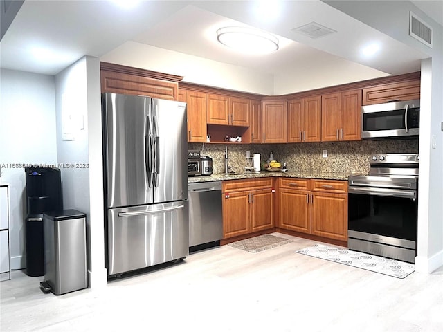 kitchen with sink, light hardwood / wood-style flooring, appliances with stainless steel finishes, light stone countertops, and decorative backsplash