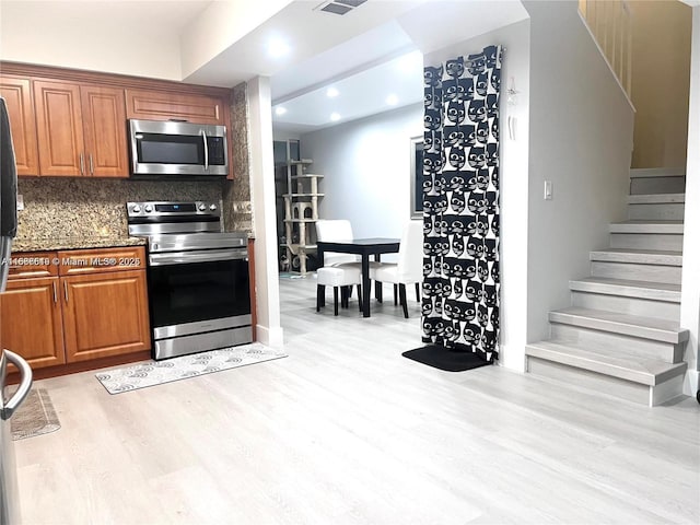 kitchen featuring appliances with stainless steel finishes, light hardwood / wood-style floors, dark stone counters, and backsplash