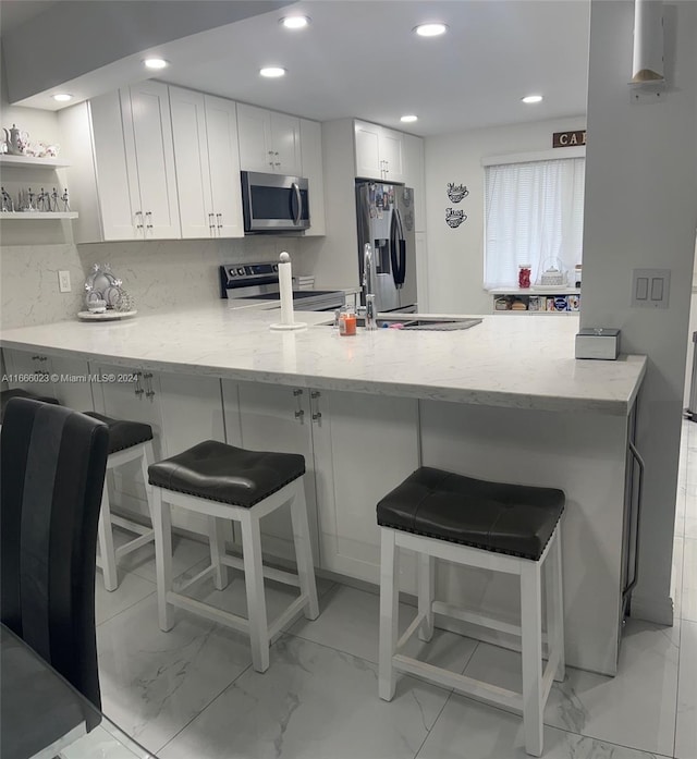 kitchen featuring light stone counters, kitchen peninsula, white cabinetry, appliances with stainless steel finishes, and a breakfast bar