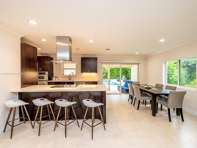 kitchen with island range hood, ornamental molding, sink, a breakfast bar area, and kitchen peninsula