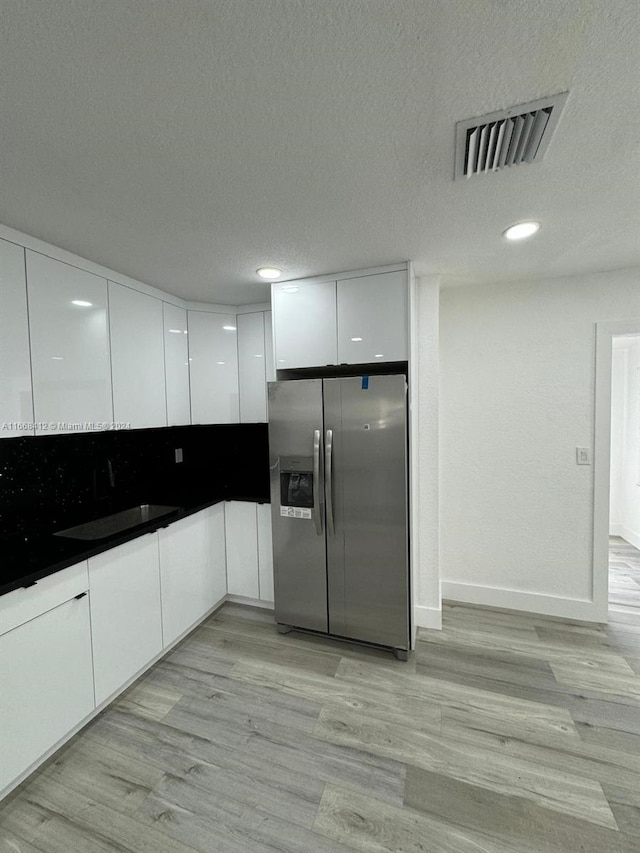 kitchen with stainless steel fridge, white cabinets, a textured ceiling, light hardwood / wood-style flooring, and sink