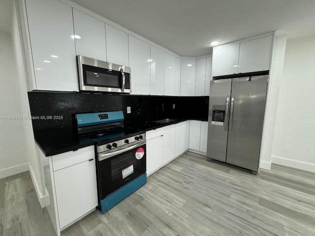 kitchen featuring sink, backsplash, white cabinetry, appliances with stainless steel finishes, and light wood-type flooring