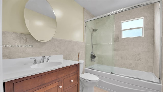 full bathroom featuring shower / bath combination with glass door, tile walls, vanity, and toilet