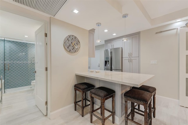 kitchen featuring a kitchen breakfast bar, hanging light fixtures, kitchen peninsula, gray cabinets, and stainless steel fridge with ice dispenser